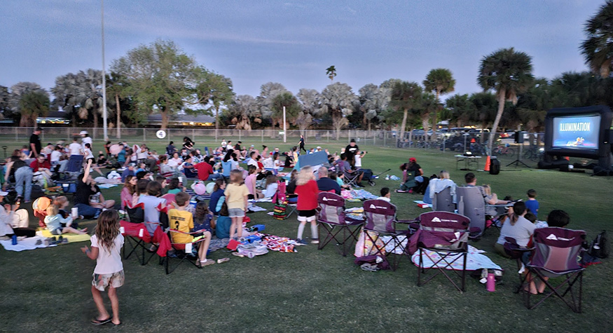 Dozens of people watching movie on inflatable projection screen at dusk