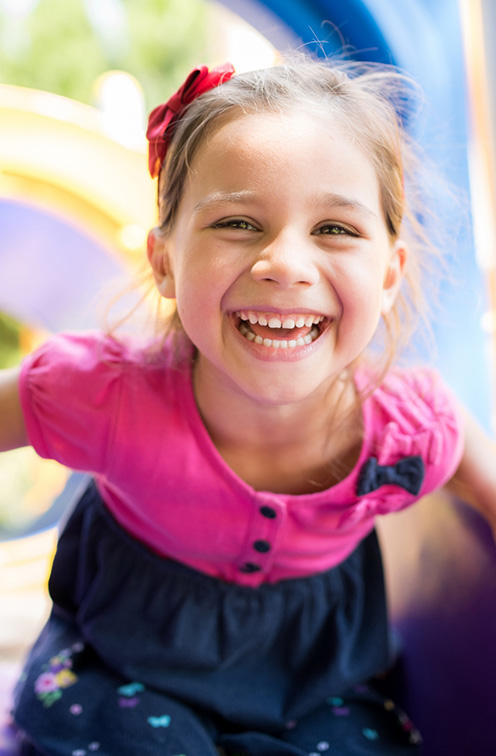 Young girl smiling on outdoor playground after seeing dentist for children in Satellite Beach