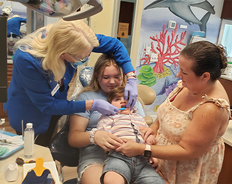 Young boy receiving dental treatment with his sister and mother supporting him