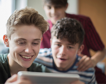 Teenage boy using tablet while two other boys watch