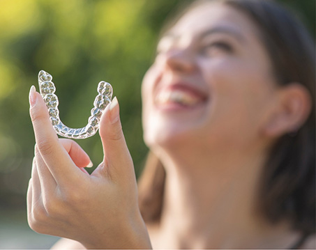 Smiling teenage girl holding an Invisalign clear aligner