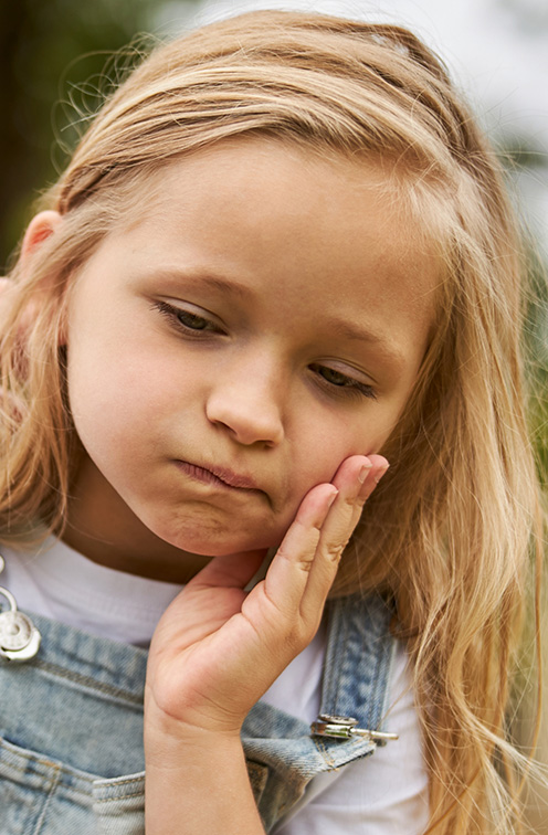 Young girl holding her cheek in pain before pediatric pulp treatment in Satellite Beach