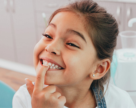 Girl in dental chair pointing to her smile