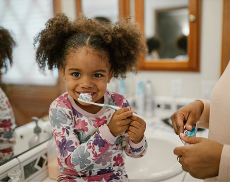 Young girl grinning while brushing her teeth