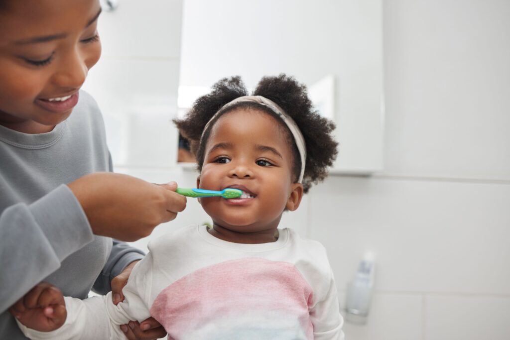 Woman brushing her toddler's teeth with blue and green toothbrush